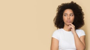 Head shot pensive thoughtful doubtful young african american lady touching chin, looking aside on empty copy space for product service promo, special offer advertising isolated on beige background.